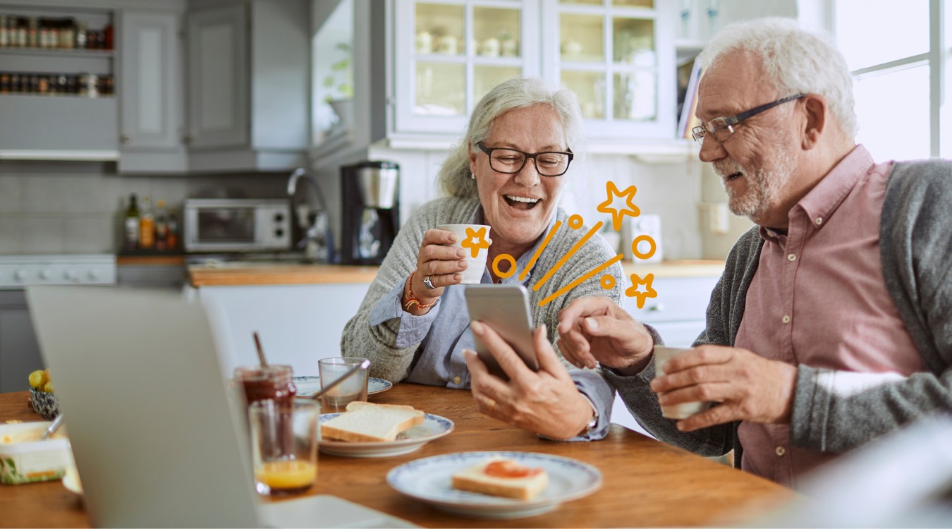 Älteres Paar sitzt am Tisch vor einem Handy