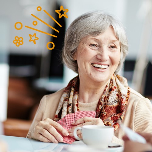 Alte Frau sitzt an einem Tisch und hält Spielkarten in der Hand