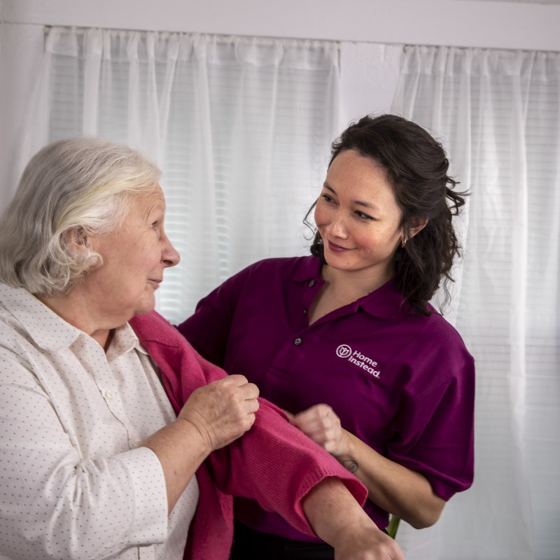Betreuerin hilft Seniorin beim Ankleiden